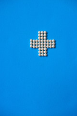 Medical cross laid out medicines, white tablets on a blue background. Pharmacology and medicine struggle for health. Drug addiction. Treatment of various diseases