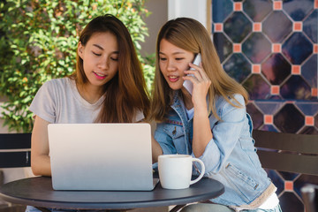 Asian young women working on laptop using and looking smartphone and drinking coffee while sitting...