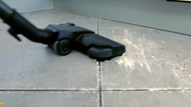 Vacuuming dirty the kitchen floor with grey tile and the corn flakes and flour scattered on the floor.