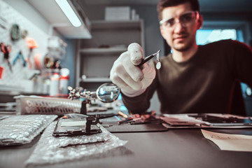 Master of electronic technology holds chip of broken tablet in the repair shop