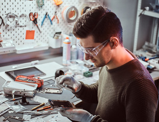 The technician uses a magnifying glass to carefully inspect the internal parts of the smartphone in...