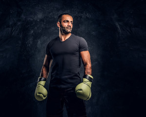 Portrait of a brutal professional fighter in a black shirt and gloves looking sideways. Studio...