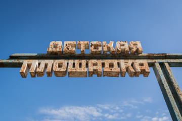 Old cracked rusty sign board in abandoned children's camp on a blue sky background