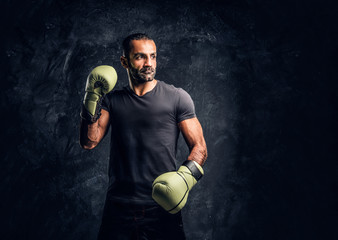 Portrait of a brutal professional fighter in a black shirt and gloves posing for a camera. Studio...
