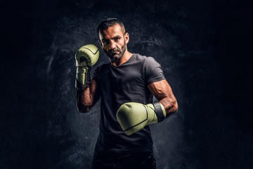 Portrait of a brutal professional fighter in a black shirt and gloves posing for a camera. Studio...