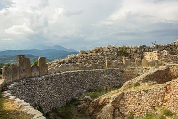 archeological dig ruins of old stone unknown city from ancient Greece time in Peloponnese peninsula area in south Europe, excavations concept, dramatic mountain landscape background, cloudy weather