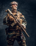 Special forces soldier in military uniform posing with assault rifle. Studio photo against a dark textured wall