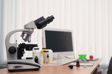 Laboratory table with microscope, flasks and a desktop computer above on a window light background. Medicine, pharmacology, pharmacy abstract background.