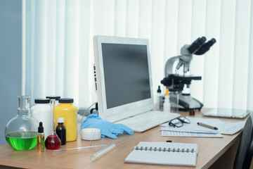 Laboratory table with microscope, flasks and a desktop computer above on a window light background. Medicine, pharmacology, pharmacy abstract background.