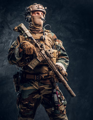 Fototapeta na wymiar Special forces soldier in military uniform posing with assault rifle. Studio photo against a dark textured wall