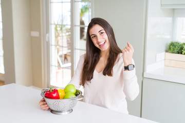 Beautiful young woman using colander to wash and clean vegatables screaming proud and celebrating victory and success very excited, cheering emotion