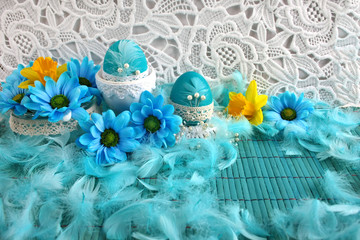 Wielkanocne biało-błękitne tło z koronką, błękitnymi pisankimi , piórami i kwiatami © Monika