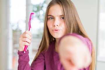 Beautiful young girl kid holding pink dental toothbrush pointing with finger to the camera and to you, hand sign, positive and confident gesture from the front