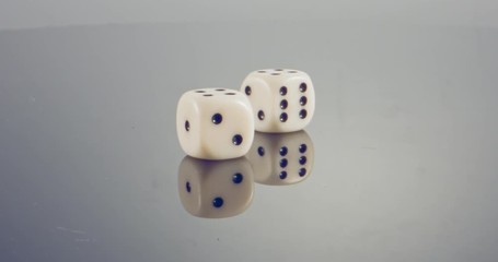 Slow motion macro shot of white dice falling and rolling on reflective surface