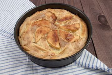 Apple pie in a baking dish on a wooden table with a striped napkin