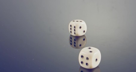 Slow motion macro shot of white dice falling and rolling on reflective surface
