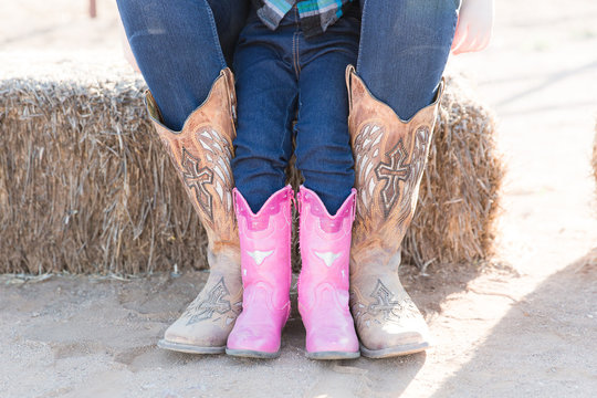 Child wearing pink cowboy boots sits with adult wearing cowboy boots