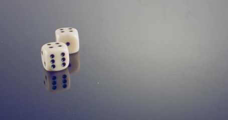Slow motion macro shot of white dice falling and rolling on reflective surface