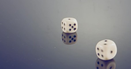 Slow motion macro shot of white dice falling and rolling on reflective surface