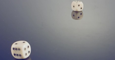 Slow motion macro shot of white dice falling and rolling on reflective surface