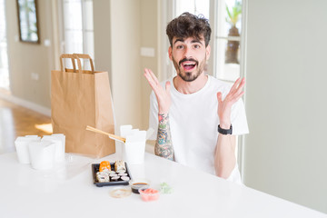Young man eating asian sushi from home delivery celebrating crazy and amazed for success with arms raised and open eyes screaming excited. Winner concept