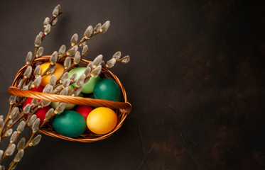 Easter eggs in a basket and willow branches on a stone background, copy space