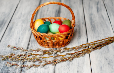 Easter eggs in a basket and willow branches on a wooden background