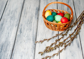 Easter eggs in a basket and willow branches on a wooden background