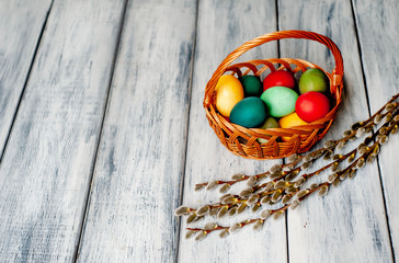 Easter eggs in a basket and willow branches on a wooden background
