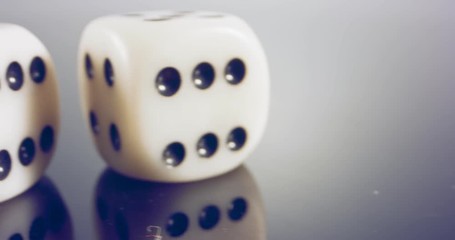 Slow motion macro shot of white dice falling and rolling on reflective surface