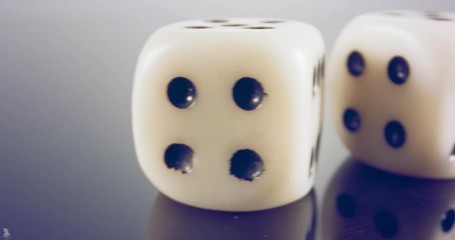 Slow motion macro shot of white dice falling and rolling on reflective surface