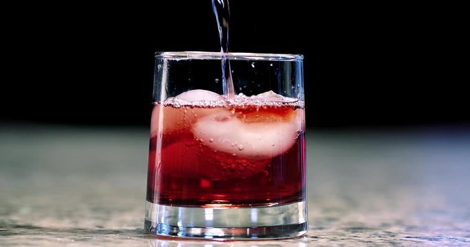 Close up of a mixed cocktail being poured into a glass and garnishing with orange