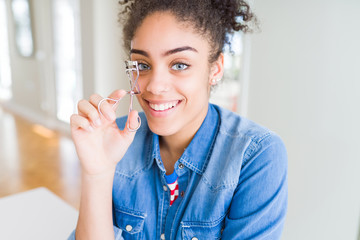 Young african american girl using eyelashes curler with a happy face standing and smiling with a confident smile showing teeth