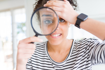 Young african american woman looking through magnifying glass stressed with hand on head, shocked...