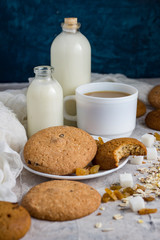 Cup of coffee with milk in a white cup, Bottles with milk, oatmeal cookies, oatmeal, raisins on a light background. Scene from breakfast