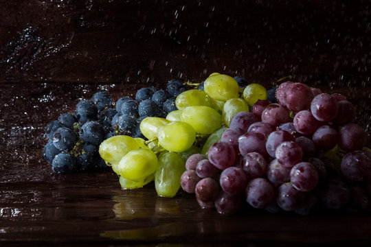 Several varieties of grapes on a wooden background with splashes of water. Fresh fruit concept, new crop