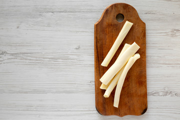 Top view, string cheese on rustic wooden board over white wooden background, top view. Healthy...