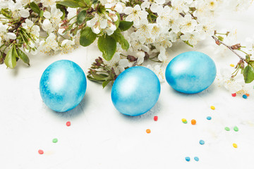 Purple blue Easter eggs, spring flowers apple, cherry, colorful candy on a white stone background