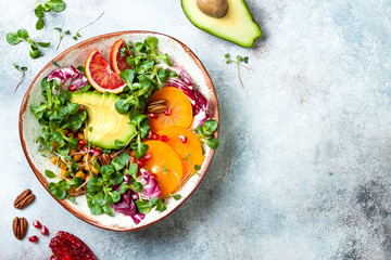 Vegan, detox Buddha bowl with turmeric roasted  chickpeas, greens, avocado, persimmon, blood orange, nuts and pomegranate. Top view, flat lay, copy space