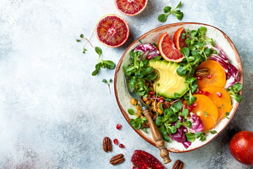 Vegan, detox Buddha bowl with turmeric roasted  chickpeas, greens, avocado, persimmon, blood orange, nuts and pomegranate. Top view, flat lay, copy space