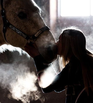 Low Key Image. Horse And Girl In Barn During Cold Winter Day, Steamy Breath Visible Back Lit From Window