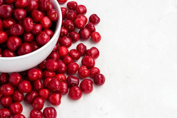 Fresh cherries in a white plate and scattered around on a light stone background