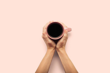 Two hands holding a cup with hot coffee on a pink background. Breakfast concept with coffee or tea. Good morning, night, insomnia. Flat lay, top view
