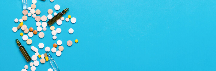 Pills of different colors and ampoules with medicine on a blue background. Concept of the...