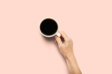 A hand is holding a cup with hot coffee on a pink background. Breakfast concept with coffee or tea. Good morning, night, insomnia. Flat lay, top view
