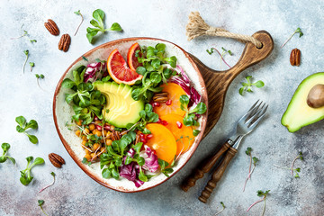 Vegan, detox Buddha bowl with turmeric roasted  chickpeas, greens, avocado, persimmon, blood orange, nuts and pomegranate. Top view, flat lay