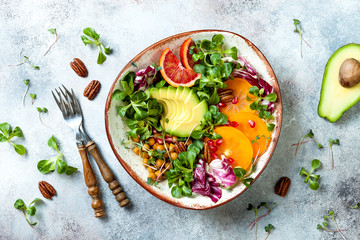Vegan, detox Buddha bowl with turmeric roasted  chickpeas, greens, avocado, persimmon, blood orange, nuts and pomegranate. Top view, flat lay