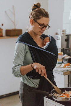 Mother with baby in baby sling cooking