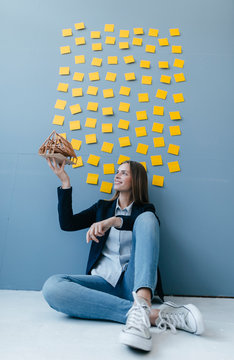 Young businesswoman holding architectural model with yellow sticky notes on the wall behind ger