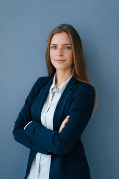 Portrait of a young businesswoman against blue background, with arms crossed